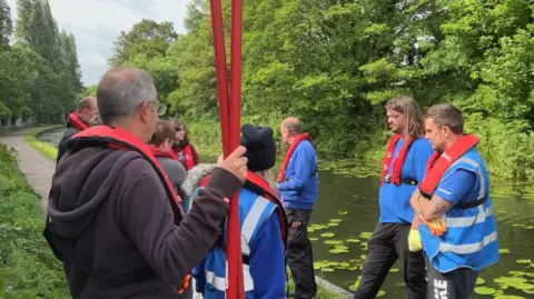 Group of people in blue jumpers with red life jackets on standing in a circle like formation.