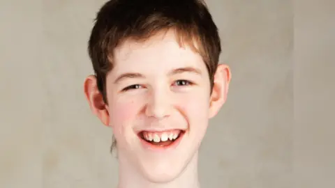 A teenage boy with short brown hair, smiling and looking directly at the camera