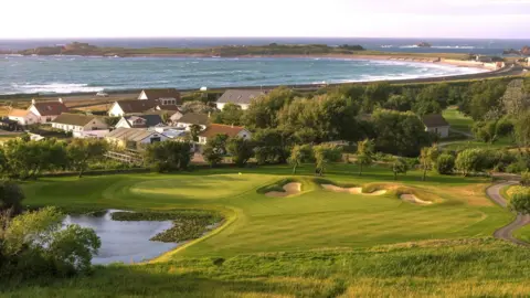 La Grande Mare An image of La Grande Mare golf course - the sea is in the background as well as houses. The golf course has sand bunkers and a pond