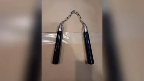 Northumbria Police A set of nunchakus placed on a table. They comprise a silver chain with two black handles.