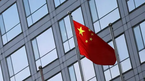 A Chinese flag on a pole, fluttering against a grey building