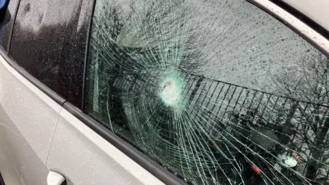 The side view of a white car with the rear passenger side window smashed