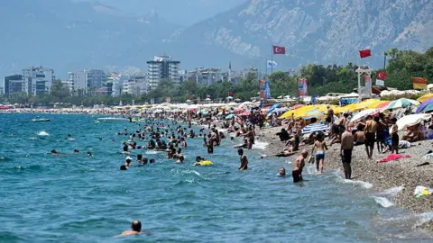 A beach in Turkey where lots of people are sunbathing under umbrellas, and many other people are swimming in the sea