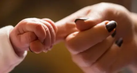 A baby holds onto the finger of a woman who has painted nails.