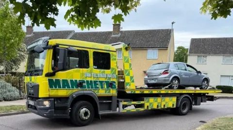 A silver car on the back of a recovery truck.