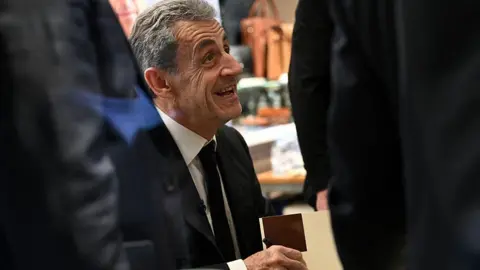 AFP via Getty Images France's former President Nicolas Sarkozy reacts as he takes part in an autograph session of his book "Diary of a Prisoner" on the day of its' release at the Lamartine bookshop in Paris on December 10, 2025. Sarkozy has written a 216-page book entitled "Diary of a Prisoner," released on December 10, 2025 and excerpts of which were published in several French media on December 6, 2025. Nicolas Sarkozy, who was president from 2007 to 2012, was protected in prison by two security officers and remained confined to his cell 23 hours a day, except for visiting hours.