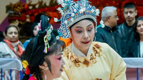 Trevor Sewell/Leicester Media Two ladies in lavish traditional Chinese dress talking, with a crowd of onlookers behind