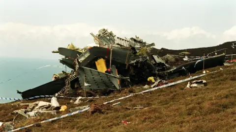 The wreckage of a military helicopter on a clifftop. The scene is cordoned off by police tape.