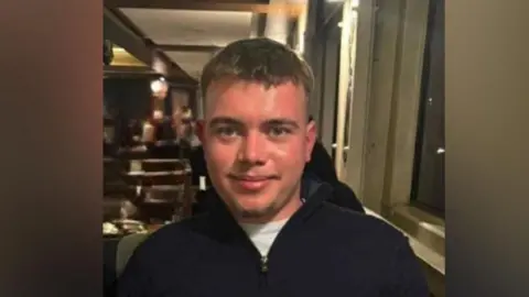 Coel Tainton is pictured looking at the camera. He has short dark hair and is wearing a black jumper with a white shirt underneath