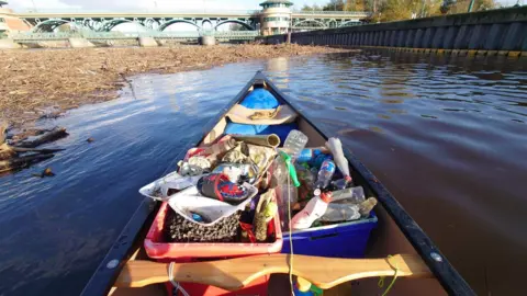 A rowing boat on the Tees filled with buckets which are overflowing with litter - most notably, an abundance of plastic bottles.