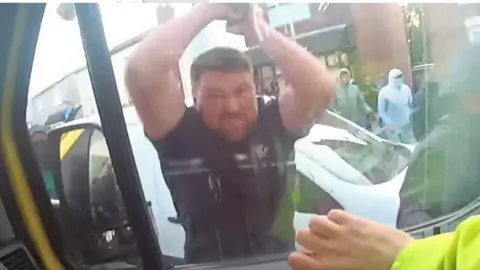 CPS Luke Moran has his hands raised in the air before he punches the driver's seat window of a police van. An officer's hand is seen inside the window, showing that someone was sitting in the driver's seat