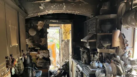 Suzanne Wright A kitchen with black soot and melted appliances and melted ceiling hanging down in the utility 