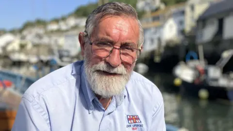 Man with grey beard and grey hair looking at the camera. He is wearing a Looe Lifeboat blue shirt.