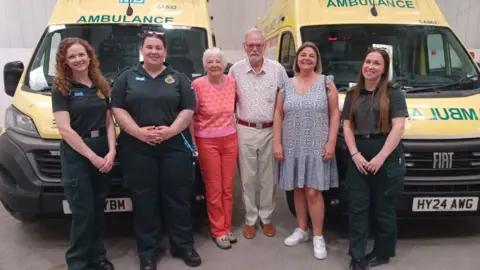 A man with his wife and daughter stood next to three female paramedics in front of two ambulances