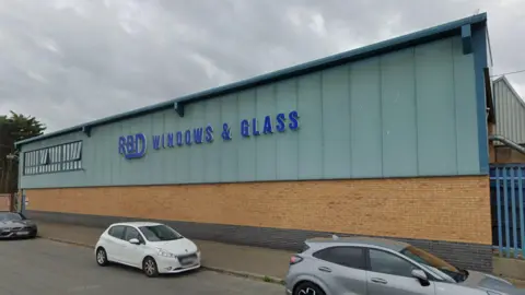 The exterior of RBD Windows and Glass. The lower half of the building is brickwork with the upper half covered in blue panelling. The company name is on the side of the building.