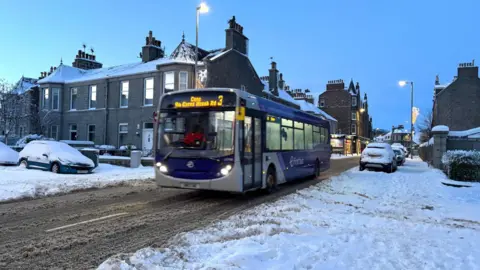 A bus driving along a street covered with snow in Aberdeen.