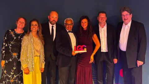 The Homeless Outreach Partnership team with their award: three women in dresses and four men in suits standing in a group holding an award