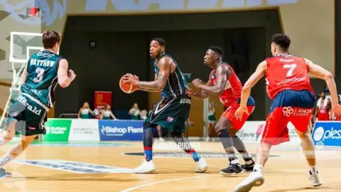 Damian Pudner Kinu Rochford holds a basketball as he is captured in motion at the centre of the court with other players around him 