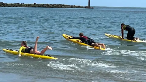 Qays Najm/BBC Three people on surfboards riding the waves of the sea at Sea Palling in Norfolk.