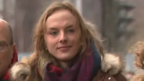 BBC Dr Beth Upton has long brown hair and has a slight smile. The medic wears a colourful scarf and a brown parka jacket