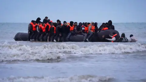 PA Media People thought to be migrants wade through the sea to board a small boat in Gravelines, France.