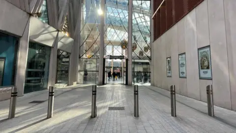 Hana Kelly/BBC A modern shopping centre with lots of glass and light-coloured concrete. The sun is shining through large windows.