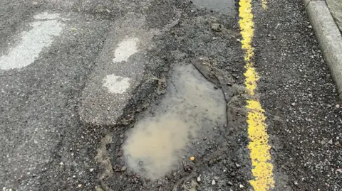 A pothole filled with water next to a yellow line at the edge of the road