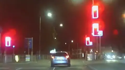 Cambridgeshire Constabulary A silver car is driven through a junction where three traffic lights are all showing red. It is night time.