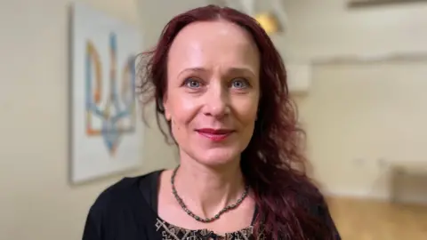 Iryna is wearing a necklace and cardigan