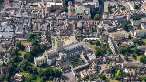 An aerial shot of Gloucester city centre on a sunny day, including Gloucester Cathedral in the foreground, green spaces, Georgian buildings, and Shire Hall