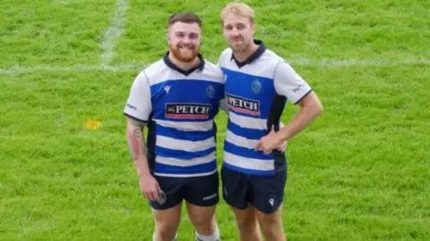 Darlington Mowden Park RFC (L-R) Sam Clay and Josh Ree, who are both dressed in rugby kit, stand together on the pitch. Sam has a short beard and Josh has blond hair.