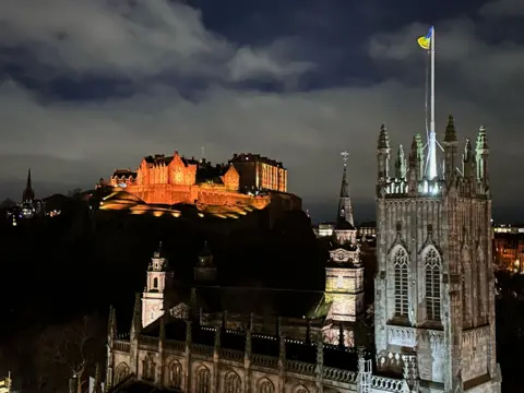Alan Jenkins Night image of Edinburgh castle, illuminated in St John's church in the foreground, illuminated.the background with  the distance 
