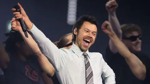 Harry Styles, who has styled short brown hair, performing in a white shirt and grey tie on stage at the BRIT awards earlier this year