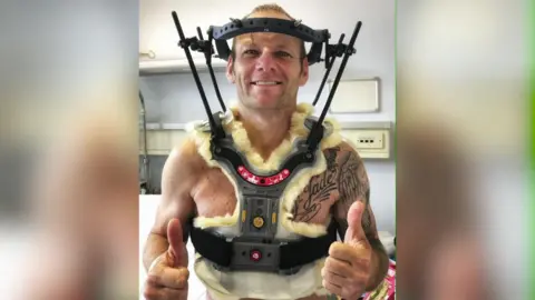 Shane Byrne poses for a picture with a piece of health equipment over his head and body,
