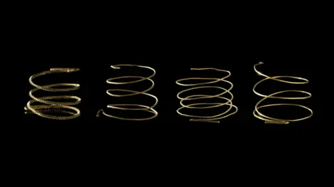 South Wales Police A hoard of four Middle Bronze Age gold armlets from Llanwrthwrl, Powys, pictured against a black backdrop.