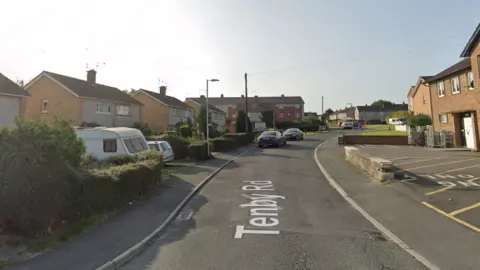 Google A Google Streetview of Tenby Road. There is a small carpark/loading bay on the right of the picture, and houses with driveways to the left.