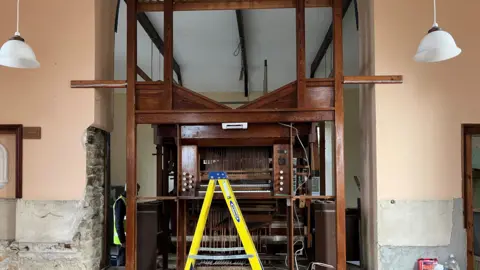 Organ with its pipes removed and a ladder in front 