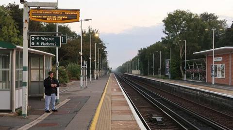 A lone passenger waiting at an empty Hassocks station, with a cancelled train sign above
