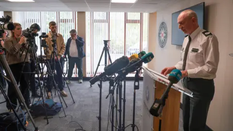 A senior PSNI officer addresses reporters and camera crews during a press conference.