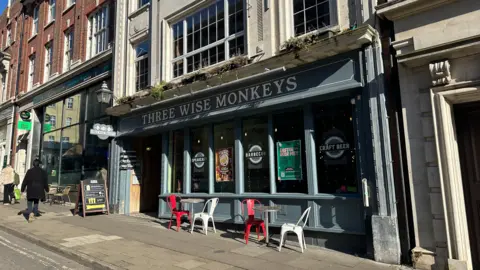 Alice Cunningham/BBC A general view of the outside of Three Wise Monkeys in Ipswich. Chairs and tables sit outside the pub which has large windows. Signage has been placed on the inside the window.