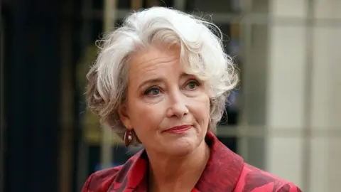 Reuters Close up of Emma Thompson from the shoulders up, who has short, white hair and is wearing a red patterned jacket.