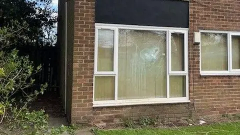 Sam Smith A large ground floor window. The glass has been shattered, likely by a thown object.