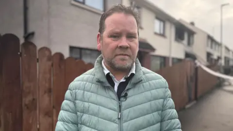 David Thompson wearing a sage green puffer jacket and white collared shirt underneath.