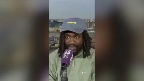 A man with shoulder-length dark hair talks into a microphone