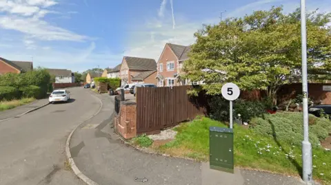 A street view of May Close in Swindon, showing a curved road with cars parked by the curb, next to rows of houses and some trees. A standard residential street.