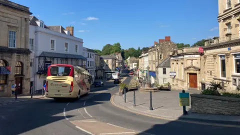 A general shot of Frome town centre taken on a sunny day. It shows shoppers and traffic.