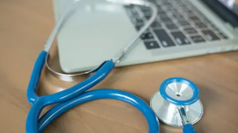 Getty Images A doctor's desk with a blue stethoscope and laptop.