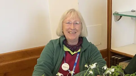 A woman sat in front of a plant on a table.