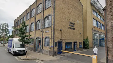 Google An exterior image of the Thames Wharf Studios, a brick building, set over three levels, with blue windows.