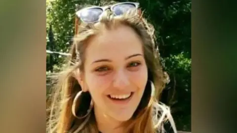 Handout Ms Espirito Santo with blonde hair with gold hoop earrings and glasses on her head smiling into the camera